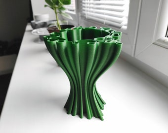 May include: A green 3D printed vase with a unique, organic design. The vase has a wide opening and a narrow base, and it is made of a smooth, textured material.