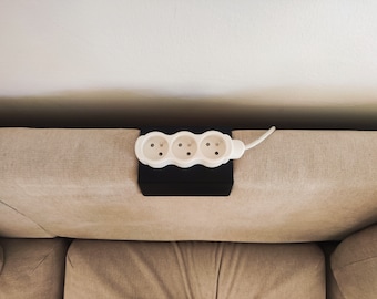 May include: A white three-outlet power strip mounted on a black surface, with a white cord extending to the right.