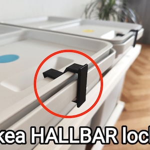 Può includere: Primo piano di un cassetto bianco con una serratura in plastica nera. La serratura è etichettata "IKEA HALLBAR lock".