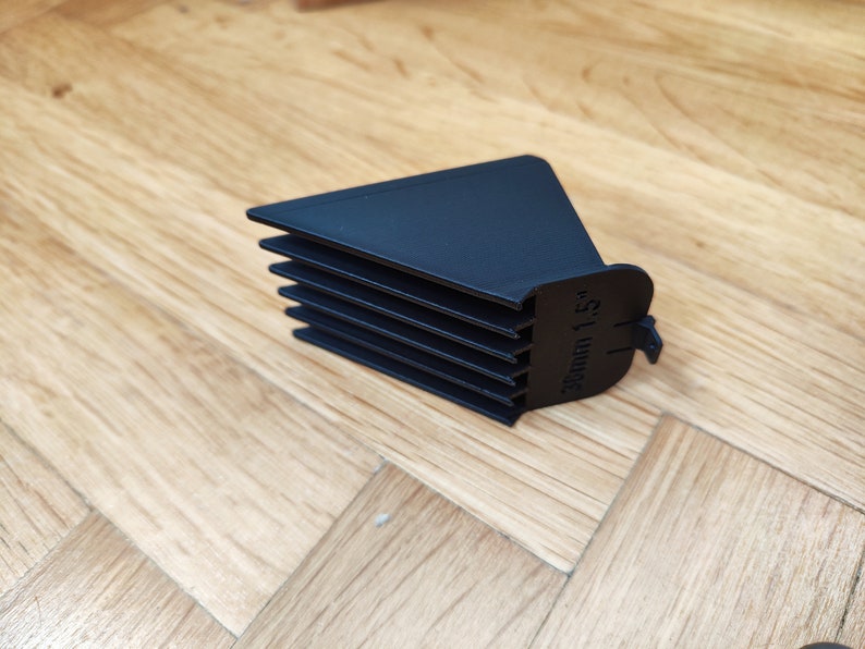 May include: Black plastic hair clipper guard with a comb attachment. The guard has a label that reads "38mm 1.5".