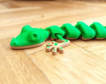 May include: A green and brown segmented toy shaped like a gecko lizard. The toy is made of plastic and has a segmented body with a tail.