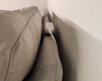 May include: A white power strip with a black cord is tucked behind a beige couch.