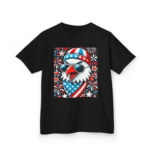 Op de afbeelding: Zwart T-shirt met een cartoon afbeelding van een adelaar die een zonnebril en een bandana met sterren en strepen draagt. De adelaar is omringd door vuurwerk en sterren.