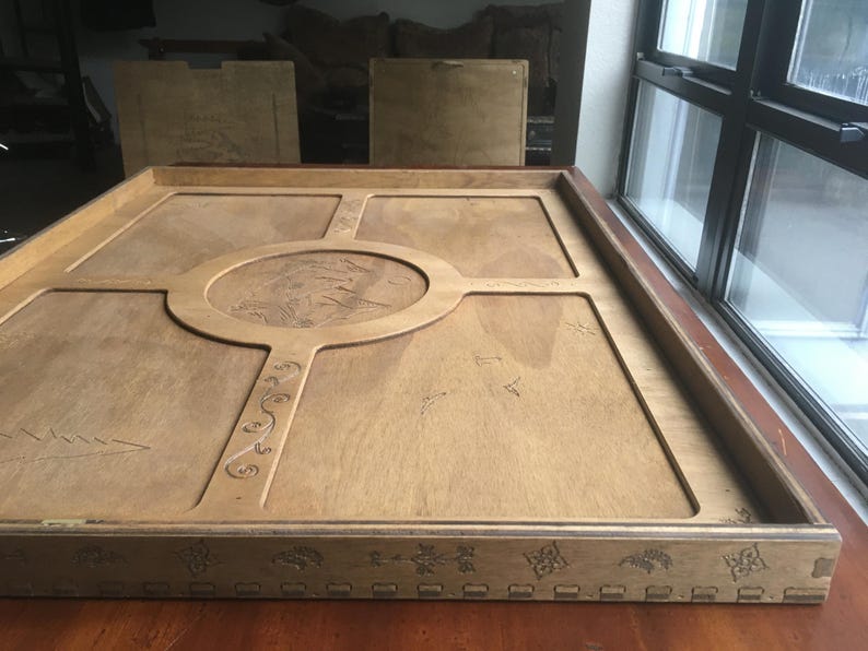 May include: A large, rectangular wooden tray with a light brown finish. The tray features a central circular design and decorative carvings. The edges are framed with detailed patterns. The tray is placed on a wooden surface.