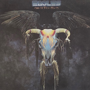 May include: Album cover art for "Eagles - One of These Nights." The image features a stylized skull with horns, adorned with feathers and tribal designs. Dark wings are spread behind the skull, with the band's name and album title at the top.