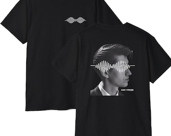 May include: A black short-sleeve t-shirt featuring a small white soundwave graphic on the front chest. The back displays a large black and white profile portrait of Alex Turner with a white soundwave graphic over the eyes and his name printed below.
