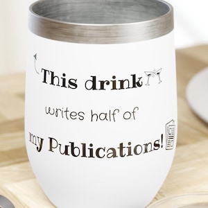 May include: White stainless steel wine tumbler with a silver rim and a black inscription that reads "This drink writes half of my publications!" The tumbler is sitting on a wooden surface with a corkscrew and a clear lid.