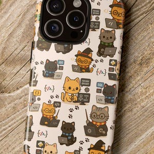 Puede incluir: Una funda de teléfono blanca con un patrón repetido de gatos de dibujos animados con gafas, sombreros y bufandas, trabajando en computadoras portátiles. El diseño incluye símbolos de código y huellas de patas. La funda está sobre una superficie de madera.