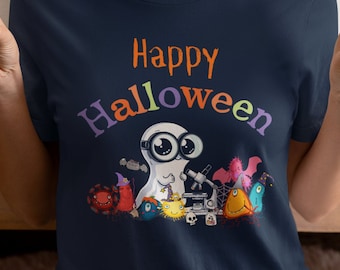 Può includere: Una maglietta blu navy con il testo "Happy Halloween" in colori arcobaleno. Un fantasma dei cartoni animati con gli occhiali sta guardando attraverso un microscopio con altre creature di Halloween intorno a lui.