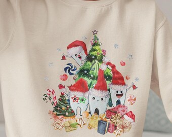 May include: A cream-coloured sweatshirt with a Christmas-themed design. The graphic depicts cartoon teeth wearing Santa hats, a decorated Christmas tree, and wrapped presents. The design is in a watercolour style, with candy canes and gingerbread biscuits.