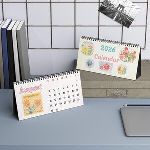 May include: Two desk calendars with spiral binding. One calendar displays the month of August with a cartoon giraffe and the text "Summer Science Fair". The other calendar is labeled "2026 Calendar" with cartoon illustrations.