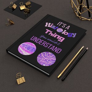 May include: Black notebook with the text "It's a Histology Thing you wouldn't understand". The notebook has two pink and purple microscope slides on the cover.