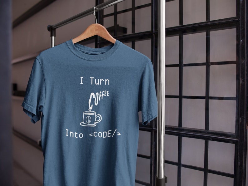 Może przedstawiać: Niebieska koszulka z białym nadrukiem przedstawiającym kubek kawy i tekst "I Turn Coffee Into  <CODE/>"