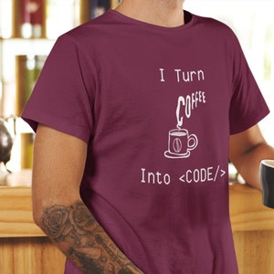 Może przedstawiać: Bordowy t-shirt z nadrukiem "I Turn Coffee Into <CODE/>" na przodzie. Tekst jest biały i przedstawia stylizowaną filiżankę kawy z unoszącą się parą.