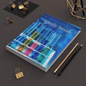 May include: A white notebook with a blue background and colourful test tubes. The notebook has the name "Emily Smith" printed on the cover.