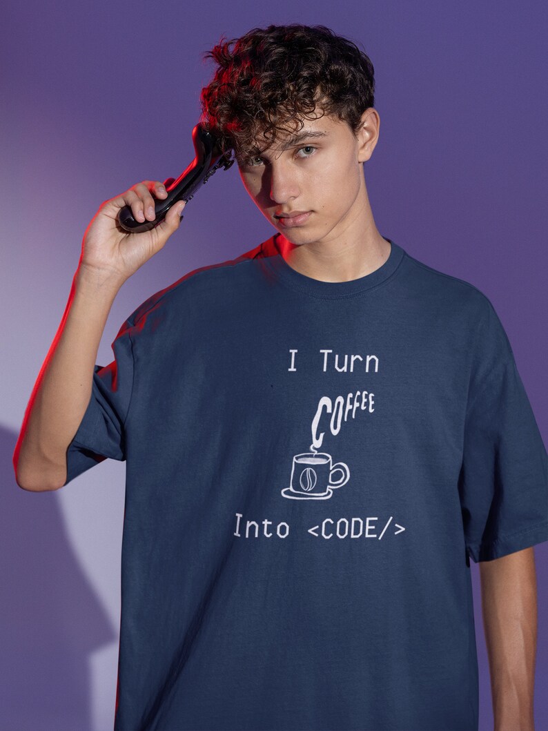 Może przedstawiać: Koszulka w kolorze granatowym z białym nadrukiem, na kt&oacute;rym widnieje napis "I Turn Coffee Into <CODE/>" wraz z kresk&oacute;wkową filiżanką kawy i parą.