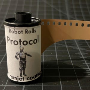 May include: A roll of 35mm film with a label that says "Robot Rolls Protocol" and features a robot character. The label also says "remjet coating".
