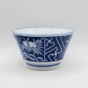 May include: A blue and white ceramic bowl with a flared shape. The bowl features a detailed design of fruit and geometric patterns. The interior and rim are white, while the exterior is decorated with blue motifs. The bowl is approximately 4 inches in diameter.