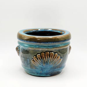 May include: A small, ceramic planter with a blue and brown glaze. The planter features a seashell design and two small handles. The rim is brown, and the body is a mix of blue and green. The planter is approximately 4 inches in diameter and 3 inches tall.