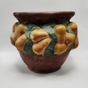 May include: A brown ceramic planter with a wide rim and a rounded body. The planter is decorated with relief-style pears and green leaves. The pears are yellow and brown, and the leaves are green. The planter is suitable for indoor or outdoor use.