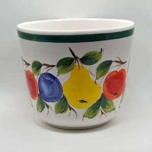 May include: White ceramic planter with a green rim and a colorful fruit design. The design includes a yellow pear, red apple, blue plum, and green leaves. The planter is a cylindrical shape.