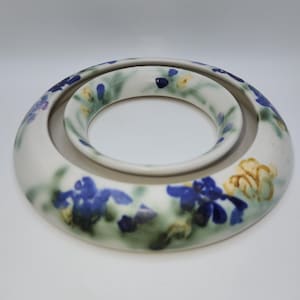 May include: A white ceramic decorative bowl with a circular design. The bowl features blue and yellow floral patterns with green accents. The inner bowl is smaller and also circular. The design is hand-painted.