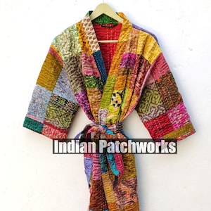 May include: A colorful patchwork robe with a tie belt. The robe is made of a variety of fabrics in different colors and patterns. The robe is hanging on a hanger against a white wall. The text "Indian Patchworks" is visible on the robe.