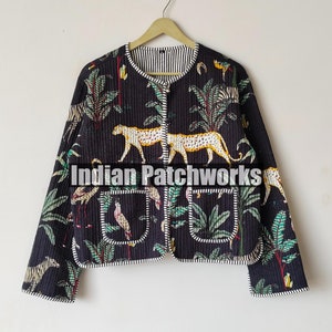 May include: A black quilted jacket with a jungle print featuring tigers, birds, and foliage. The jacket has a round neckline, two front pockets, and a striped lining. The jacket is hanging on a wooden hanger.
