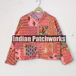 May include: A pink patchwork jacket with various patterns, including floral and geometric designs. The jacket has long sleeves and a collared neckline. The text "Indian Patchworks" is across the front.
