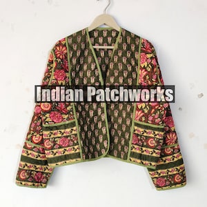 Może przedstawiać: Oliwkowozielona pikowana kurtka z kwiatowymi i paisley wzorami w kolorze różowym, żółtym i zielonym. Kurtka ma dekolt w serek, długie rękawy i kontrastowe zielone wykończenie. Z przodu widnieje napis "Indian Patchworks".