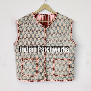 May include: A cream-colored quilted vest with a floral print and red and blue trim. The vest has two pockets and a button closure. The text "Indian Patchworks" is printed on the front of the vest.