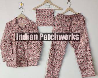May include: A three-piece pajama set in a pink and white teardrop pattern. The set includes a button-down shirt, a pair of pants, and a matching eye mask, all hanging on wooden hangers. The text "Indian Patchworks" is visible.