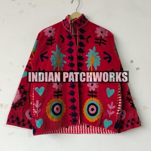 Pode incluir: Uma jaqueta vermelha com bordados coloridos de flores e corações em tons de azul, rosa e amarelo. A peça possui gola alta, mangas compridas e forro listrado de vermelho e branco. O texto INDIAN PATCHWORKS é visível.