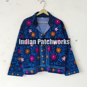 May include: A dark blue jacket with floral embroidery in pink, orange, and blue. The jacket has a striped lining and is buttoned up. The text "Indian Patchworks" is across the bottom of the jacket.