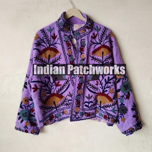 May include: A purple embroidered jacket with floral patterns in shades of brown, blue, and green. The jacket has a mandarin collar and a button closure. The text "Indian Patchworks" is visible on the front of the jacket.