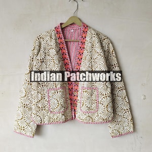 May include: A white cotton jacket with a pink and white striped lining. The jacket has a floral pattern and a pink trim. The jacket is hanging on a hanger against a white wall. The text "Indian Patchworks" is visible on the jacket.