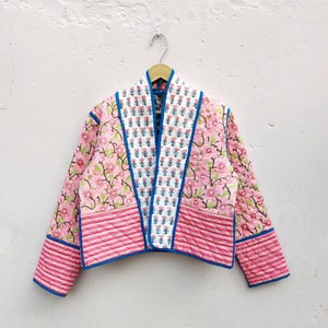 May include: A pink and white quilted jacket with blue trim. The jacket has a floral print and a striped pattern.