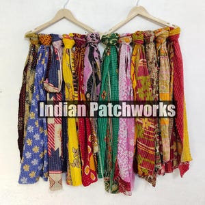 Puede incluir: Una colecci&oacute;n de coloridas bufandas estampadas colgadas de perchas de madera. Las bufandas muestran una variedad de dise&ntilde;os, incluyendo patrones florales y geom&eacute;tricos, en tonos de azul, amarillo, rojo y verde. El texto "INDIAN PATCHWORKS" es visible.
