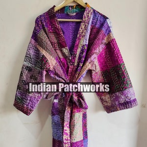 Pode incluir: Uma bata acolchoada de patchwork roxo e rosa com cinto para amarrar. A bata é feita de tecido kantha e tem um visual vintage. "Indian Patchworks" está impresso na bata.