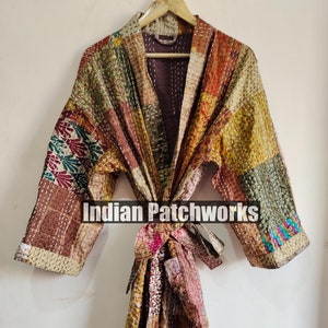 May include: A long, brown, patchwork robe with a tie belt. The robe is made of different fabrics and has a variety of colors, including red, green, blue, and yellow. The robe is hanging on a wooden hanger. The text "Indian Patchworks" is printed on the robe.
