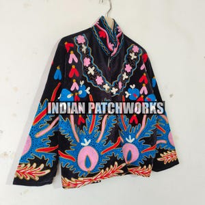 May include: A black jacket featuring vibrant, multi-colored floral and leaf embroidery in shades of blue, pink, red, and white. The garment has a high collar and long sleeves, with the text INDIAN PATCHWORKS printed across the center front.