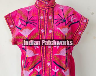 May include: A vibrant pink embroidered jacket with a high collar and short sleeves. The jacket features intricate floral embroidery in shades of purple, green, and yellow. The text "Indian Patchworks" is across the front. The jacket has matching pink ties.
