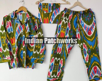 Peut inclure: Un ensemble de pyjama vert avec un motif ikat coloré, comprenant une chemise boutonnée, un pantalon et une pochette assortie. Le motif présente des accents bleus, rouges et jaunes. L'ensemble est présenté sur des cintres en bois sur fond blanc.