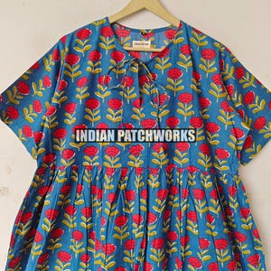May include: A blue dress featuring a red floral print and the text "INDIAN PATCHWORKS". The dress has short sleeves and a tie at the neckline. The floral pattern includes red flowers and green leaves.