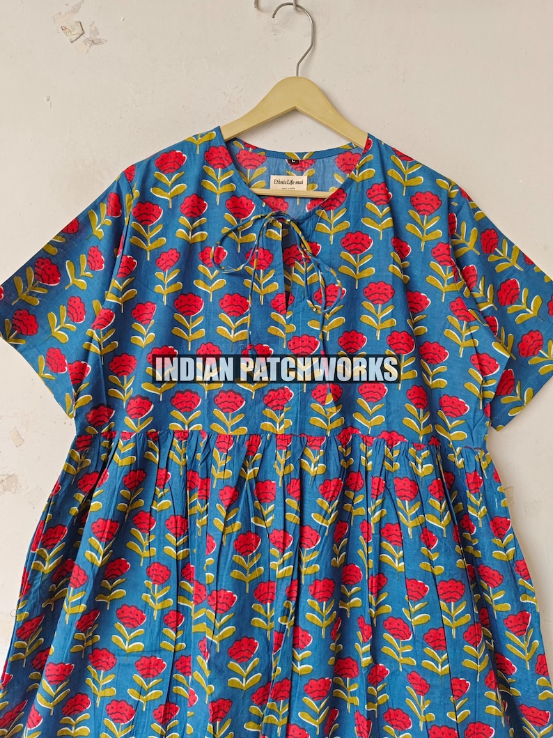 May include: A blue dress featuring a red floral print and the text "INDIAN PATCHWORKS". The dress has short sleeves and a tie at the neckline. The floral pattern includes red flowers and green leaves.