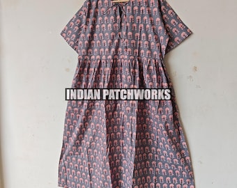 Puede incluir: Un vestido gris con un estampado floral rosa, mangas cortas y un detalle de cuello anudado. El vestido está colgado de una percha de madera. El texto "INDIAN PATCHWORKS" está impreso en el vestido.