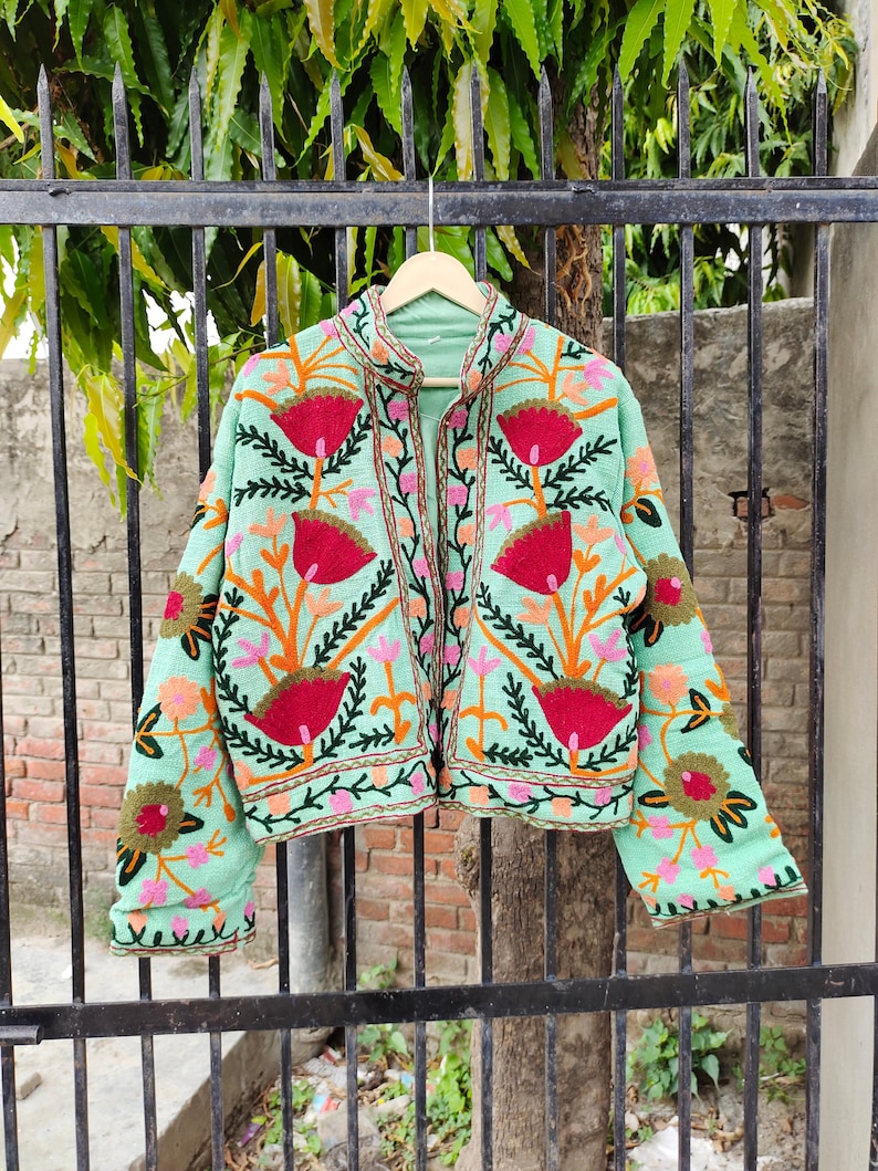 May include: A mint green embroidered jacket with floral patterns in shades of pink, red, orange, and green. The jacket has a mandarin collar and a front zipper closure.