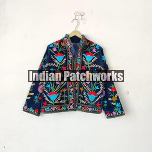 May include: A navy blue velvet jacket with colorful floral embroidery. The jacket has a mandarin collar and long sleeves. The embroidery features a variety of flowers, leaves, and vines in shades of red, pink, yellow, blue, and green. The text "Indian Patchworks" is visible on the jacket.