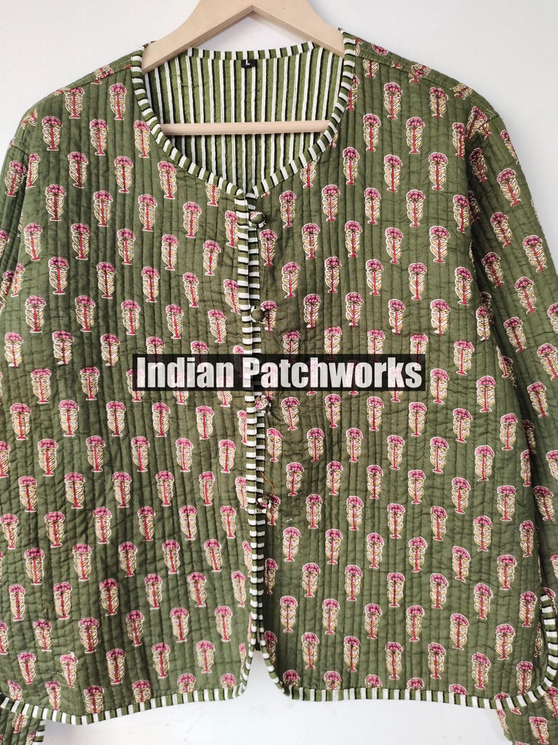 May include: Olive green quilted jacket with a floral pattern in pink and beige. The jacket features a striped lining and trim, with a button-up front. The text "Indian Patchworks" is visible on the front.