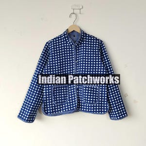 May include: A blue and white checkered jacket with long sleeves and two front pockets. The jacket is hanging on a wooden hanger against a white wall. The text "Indian Patchworks" is across the front of the jacket.